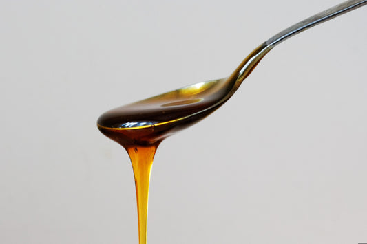 A close-up of a spoon filled with dark, amber-colored mad honey, slowly dripping off the edge against a neutral background