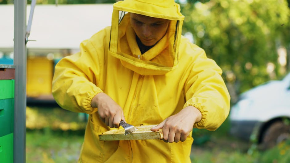 A beekeeper in a yellow outfit harvesting honey outdoors on a sunny day.